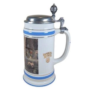 May include: White ceramic beer stein with a metal lid and handle. The stein features blue stripes and a detailed image on the front. The stein has the words "DINKEL ACKER" in gold lettering.