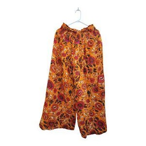 K&ouml;nnte beinhalten: Eine orangefarbene Hose mit weitem Bein und einem Blumenmuster in Rot, Rosa und Schwarz. Die Hose h&auml;ngt an einem wei&szlig;en Kleiderb&uuml;gel vor wei&szlig;em Hintergrund. Der Bund ist elastisch.