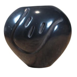 May include: A dark gray ceramic vase with a glossy finish. The vase has a rounded shape with a wide opening and a series of carved, elongated openings on the side, creating a decorative pattern. The vase is a decorative home accent.