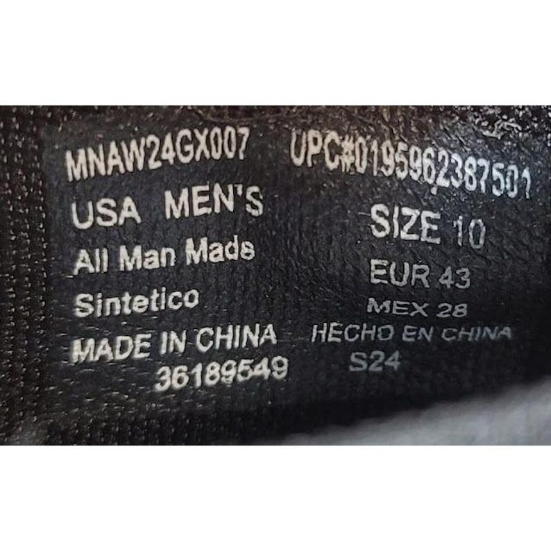 May include: Close-up of a black shoe label with white text. The label includes the text "USA MEN'S", "SIZE 10", and "MADE IN CHINA". Other text includes "All Man Made" and "Sintetico".