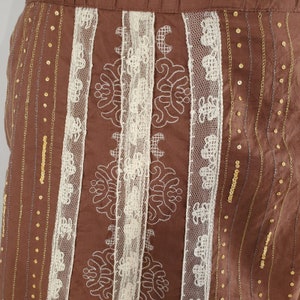Peut inclure: Jupe marron avec dentelle blanche et paillettes dor&eacute;es. La jupe a un motif vertical de dentelle et de paillettes.