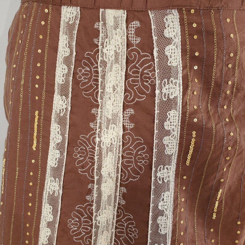 Peut inclure: Jupe marron avec dentelle blanche et paillettes dor&eacute;es. La jupe a un motif vertical de dentelle et de paillettes.