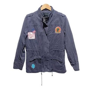 May include: A navy blue jacket with various patches, including an American flag and a cactus design. The jacket features a stand-up collar, two front pockets, and a drawstring waist. The word "Cruise" is visible on one of the patches.