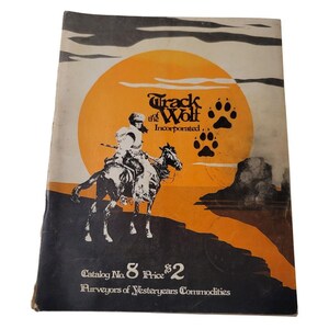 May include: A vintage catalog cover for Track of the Wolf Incorporated, purveyors of yesteryear's commodities. The cover features a black and white illustration of a Native American man riding a horse against a sunset backdrop. The text "Track of the Wolf Incorporated" is printed in black and white, along with the catalog number "8" and price "$2".