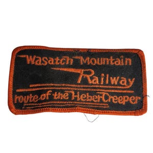 May include: A black and orange embroidered patch with the text "Wasatch Mountain Railway" and "Route of the Heber Creeper".