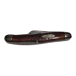 May include: A vintage Case brand pocket knife with a brown wood handle and a silver blade. The knife is closed and has a single blade.