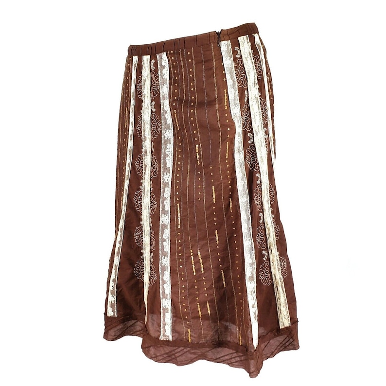 Peut inclure: Une jupe marron avec des bordures en dentelle blanche et des accents dor&eacute;s. La jupe a une silhouette fluide et &eacute;vas&eacute;e.