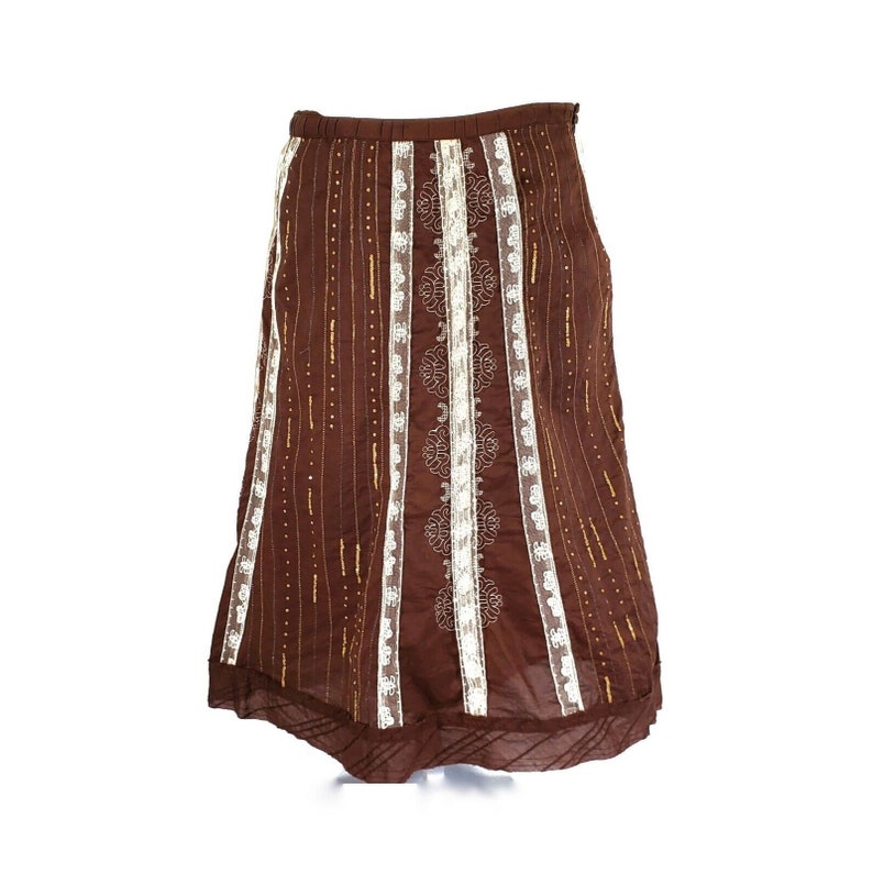 Peut inclure: Une jupe maxi marron avec des bordures en dentelle blanche et des accents dor&eacute;s. La jupe a une silhouette fluide et un design d&eacute;licat et f&eacute;minin.