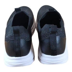 May include: Pair of black slip-on sneakers with white soles. The shoes have a textured knit upper and a pull tab at the heel. The soles are thick and white, providing a contrast to the black upper.