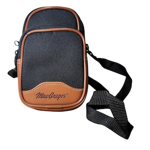 May include: Black and brown MacGregor crossbody bag with a shoulder strap. The bag has a rectangular shape with a brown leather-like trim and a brown leather-like patch at the bottom with the MacGregor logo.