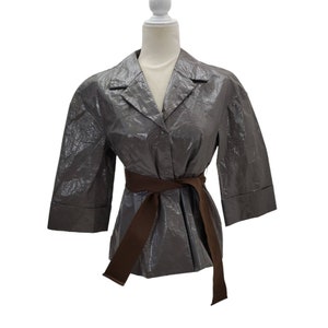 May include: A gray, shiny, belted jacket with a collar and long sleeves. The jacket has a brown belt.