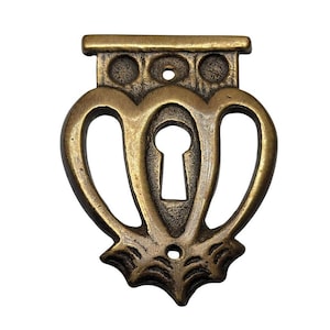 May include: Antique brass-toned keyhole cover with a decorative heart-shaped design. The cover features a keyhole in the center and a decorative top with three circular accents. The bottom has a stylized, web-like design.