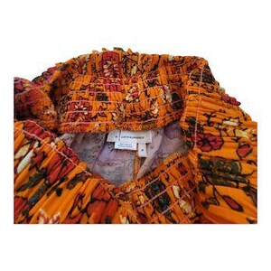 K&ouml;nnte beinhalten: Nahaufnahme einer orangefarbenen Shorts mit floralem Muster. Die Shorts haben einen gerafften Bund und ein farbenfrohes Muster aus roten, wei&szlig;en und gr&uuml;nen Blumen. Der Stoff wirkt leicht.