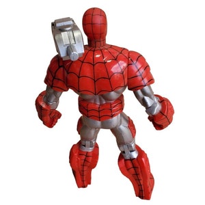K&ouml;nnte beinhalten: Eine rote und silberne Actionfigur von Spider-Man, die einen silbernen Anzug mit einem Spinnennetz-Design tr&auml;gt. Die Figur hat eine silberne Waffe, die an ihrem R&uuml;cken befestigt ist.