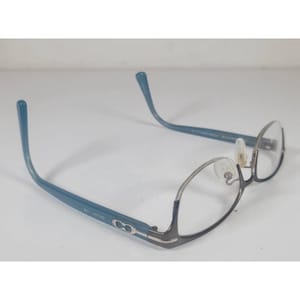 May include: Eyeglasses featuring a dark grey metal frame front and blue plastic temples. The temples display a silver-toned metallic logo detail near the hinges. The glasses include clear lenses and translucent nose pads attached to the bridge.