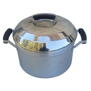 May include: A polished stainless steel stockpot with a matching lid. The pot features two black side handles and a black handle on the lid. The exterior surface is reflective and smooth, showing a cylindrical body with a slightly domed lid design.