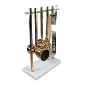 May include: A gold-toned bar tool set with a shaker, strainer, and other tools, displayed on a white marble base. The tools are arranged in a vertical rack. The set is designed for mixing cocktails.