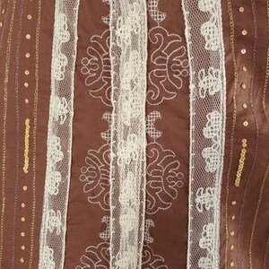 Peut inclure: Tissu brun avec bordure en dentelle blanche et paillettes dor&eacute;es. Le tissu pr&eacute;sente un motif r&eacute;p&eacute;titif de broderie blanche.