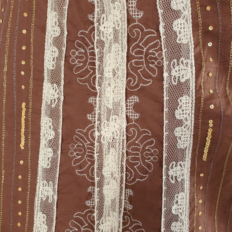 Peut inclure: Tissu brun avec bordure en dentelle blanche et paillettes dor&eacute;es. Le tissu pr&eacute;sente un motif r&eacute;p&eacute;titif de broderie blanche.
