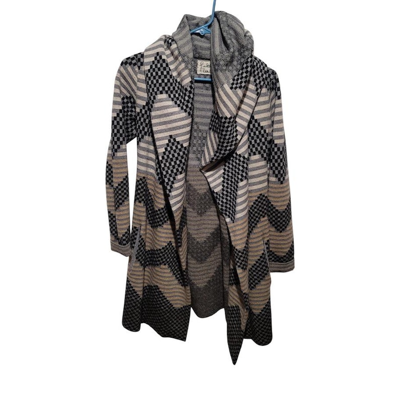 May include: A long-sleeved, black, white, and brown patterned cardigan with a hood. The cardigan has a chevron pattern and a draped front.