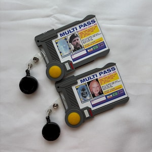 Pode incluir: Dois cartões multi-pass de plástico cinzento com cordões retráteis. Os cartões incluem uma foto, um nome e um endereço. O texto nos cartões diz "MULTI PASS" e "KORBEN DALLAS" e "LEELOO DALLAS".