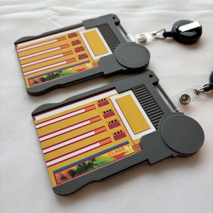 Puede incluir: Dos portagajetas de pl&aacute;stico gris con gr&aacute;ficos de barras amarillos y rojos y el texto "CLASS T" en la parte delantera. Cada portagajetas tiene un carrete de gajeta retr&aacute;ctil.