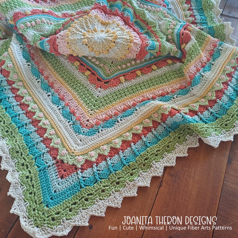 May include: A colorful, crocheted blanket with a variety of patterns and textures. The blanket features a mix of pastel colors, including green, blue, pink, and yellow. The edges are finished with a scalloped border. The text "JOANITA THERON DESIGNS" is visible.