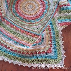 May include: A colorful, crocheted blanket with a circular design. The blanket features a variety of colors, including pink, blue, green, and yellow. The edges are scalloped, and the blanket has a textured appearance. The text "JOANITA TUEON DESIGNS" is visible at the bottom.
