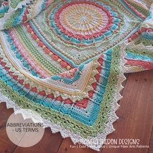 May include: A colorful, crocheted blanket with a circular design in the center. The blanket features a variety of colors, including pink, green, blue, and yellow. The text "JOANITA THERON DESIGNS" is visible at the bottom. The blanket is made with US terms.