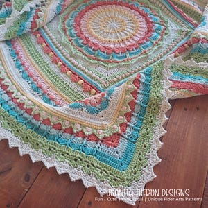 May include: A colorful, handmade crochet blanket with a circular design. The blanket features a variety of colors, including pink, green, blue, and yellow. The edges are scalloped. The text "JOANITA THERON DESIGNS" is visible at the bottom.