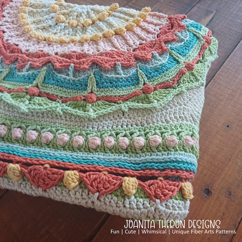 May include: A handmade crochet item in a variety of colors, including peach, teal, green, and cream. The design features intricate patterns and textures, with scalloped edges and floral accents. The text "JOANITA THERON DESIGNS" is visible at the bottom.