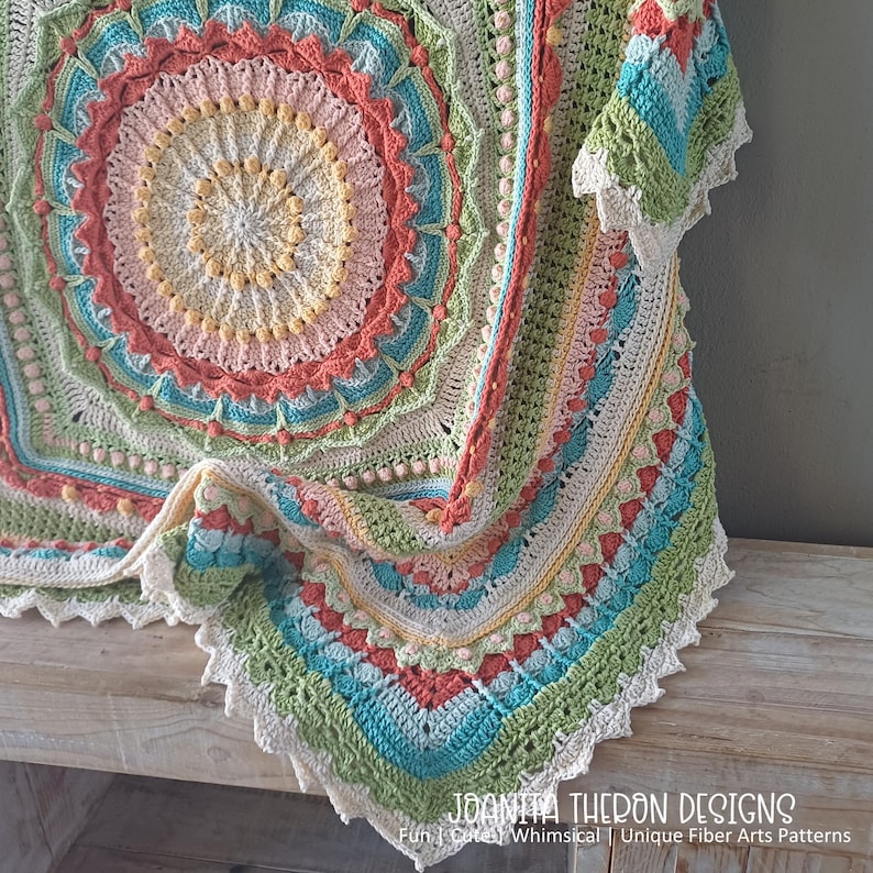 May include: A colorful, handmade crochet blanket with a circular design. The blanket features a variety of pastel colors, including pink, blue, green, and yellow, with a scalloped edge. The text "JOANITA THERON DESIGNS" is visible.
