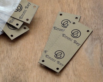May include: A stack of brown paper tags with the text "Emmi Rey" and a stylized letter "E" logo. The tags are in a white mesh bag.