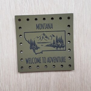 Peut inclure: Patch en cuir vert avec un contour noir de l'état du Montana, des montagnes et des arbres. Le texte "MONTANA" et "WELCOME TO ADVENTURE" est imprimé en noir.