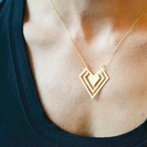 May include: A gold necklace featuring a geometric heart pendant. The pendant is crafted from three overlapping squares, creating a layered design.
