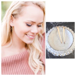 Könnte beinhalten: Ein Paar goldene Ohrringe mit einem langen, dünnen, spitzen Design. Die Ohrringe werden auf einer weißen Keramikplatte gezeigt.