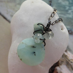 May include: A delicate necklace with a cluster of light blue and clear gemstones wrapped in wire. The necklace is made with a dark metal chain.