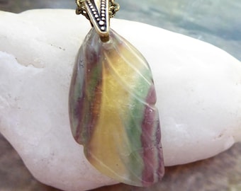 May include: A pendant carved into a leaf shape from multi-colored fluorite stone, featuring bands of yellow, green, and purple. The stone is suspended from a textured antique brass-toned metal bail and a matching link chain necklace.
