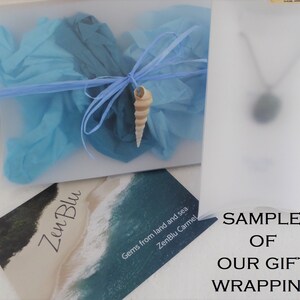 May include: A sample of gift wrapping for a necklace. The wrapping is a clear plastic bag with blue tissue paper and a seashell. The bag is labeled "ZenBlu Carmel, Gems from land and sea".