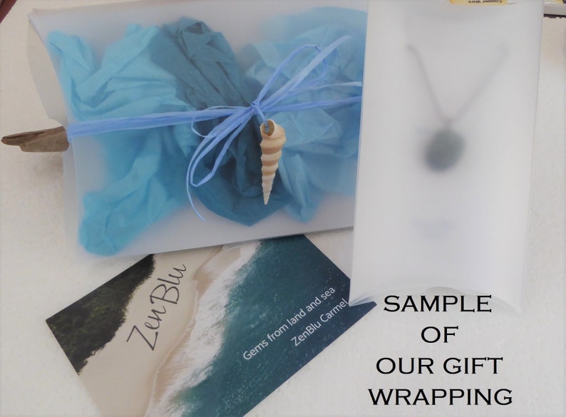 May include: A sample of gift wrapping for a necklace. The wrapping is a clear plastic bag with blue tissue paper and a seashell. The bag is labeled "ZenBlu Carmel, Gems from land and sea".