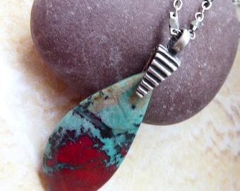 May include: A teardrop-shaped pendant featuring a polished stone with vibrant red, turquoise, and black veining. The stone is held by a textured, ridged silver-toned metal bail and hangs from a matching silver-toned chain with small, faceted links.