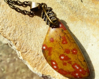 May include: A pendant necklace featuring a polished, teardrop-shaped stone with a mustard yellow base and scattered red spots with white centers. The stone is attached to a bronze-toned metal bail shaped like a leaf, hanging from a matching chain.