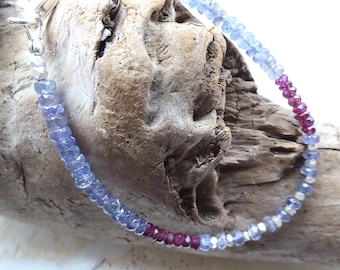 May include: A delicate beaded bracelet featuring small, faceted light blue and deep magenta gemstone beads interspersed with tiny, reflective silver-toned metal spacers. The bracelet includes a silver-toned metal clasp mechanism at one end.