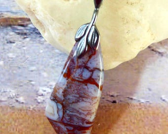 May include: A pendant necklace featuring a teardrop-shaped stone with white and deep red veined patterns. The stone is held by a silver-toned metal bail shaped like two small leaves, attached to a matching silver-toned metal link chain.