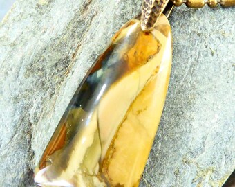 May include: A polished, triangular-shaped pendant made of tan, brown, and cream-colored stone with a smooth, glossy finish. The pendant is attached to a textured, dark bronze-toned metal bail and hangs from a matching bronze-toned ball chain.
