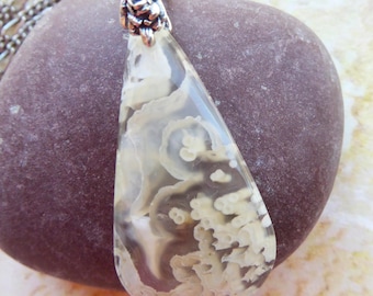 May include: A teardrop-shaped pendant featuring a translucent stone with cream-colored, organic, coral-like inclusions. The pendant is attached to a silver-toned metal bail with a floral design and hangs from a silver-toned chain necklace.