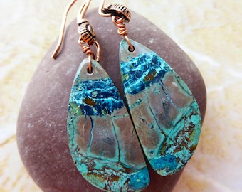 May include: A pair of teardrop-shaped earrings featuring natural stone with marbled patterns in shades of deep blue, turquoise, and brown. The stones are suspended from copper-toned metal ear wires with decorative coiled accents at the top.
