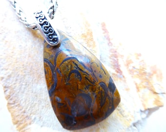 May include: A pendant necklace featuring a polished, triangular-shaped brown and black patterned stone. The stone is set in a silver-toned metal bail with an intricate, embossed scrollwork design, attached to a braided silver-toned metal chain.