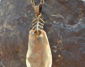 May include: A pendant necklace featuring a translucent, pale yellow, irregular teardrop-shaped stone suspended from a bronze-toned metal chain. The stone is attached to the chain by a decorative metal bail shaped like a small, textured leaf.