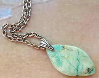 May include: A necklace featuring a teardrop-shaped, light green turquoise stone pendant with natural dark veining. The stone is held by a silver-toned metal bail and hangs from a matching silver-toned metal chain with oval-shaped links.